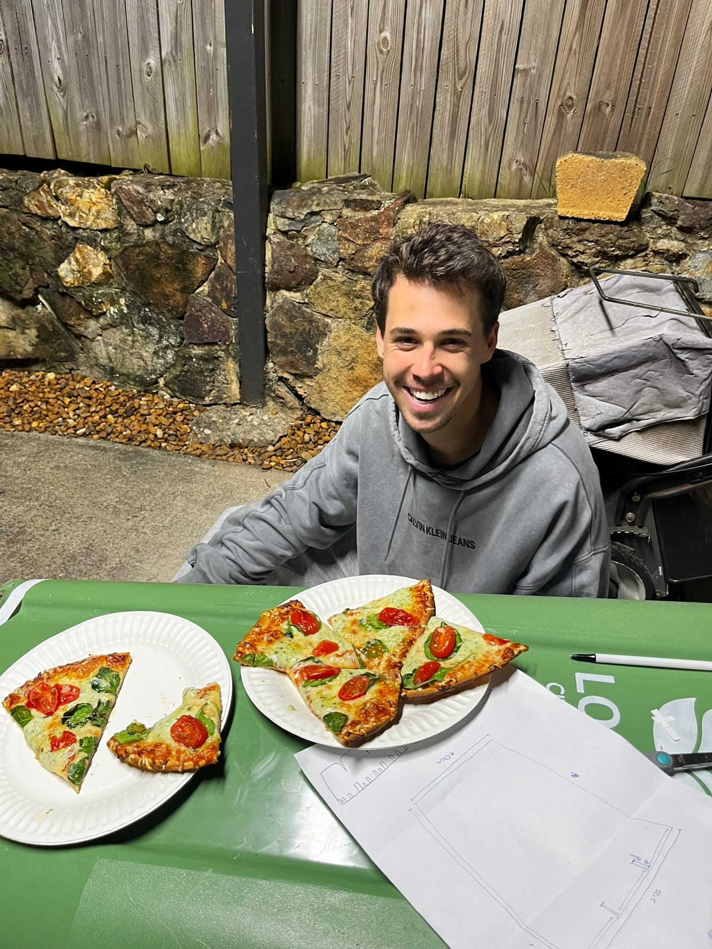 Pizza on paper plates on top of a wheelie bin, next to a hand-drawn pattern sketch